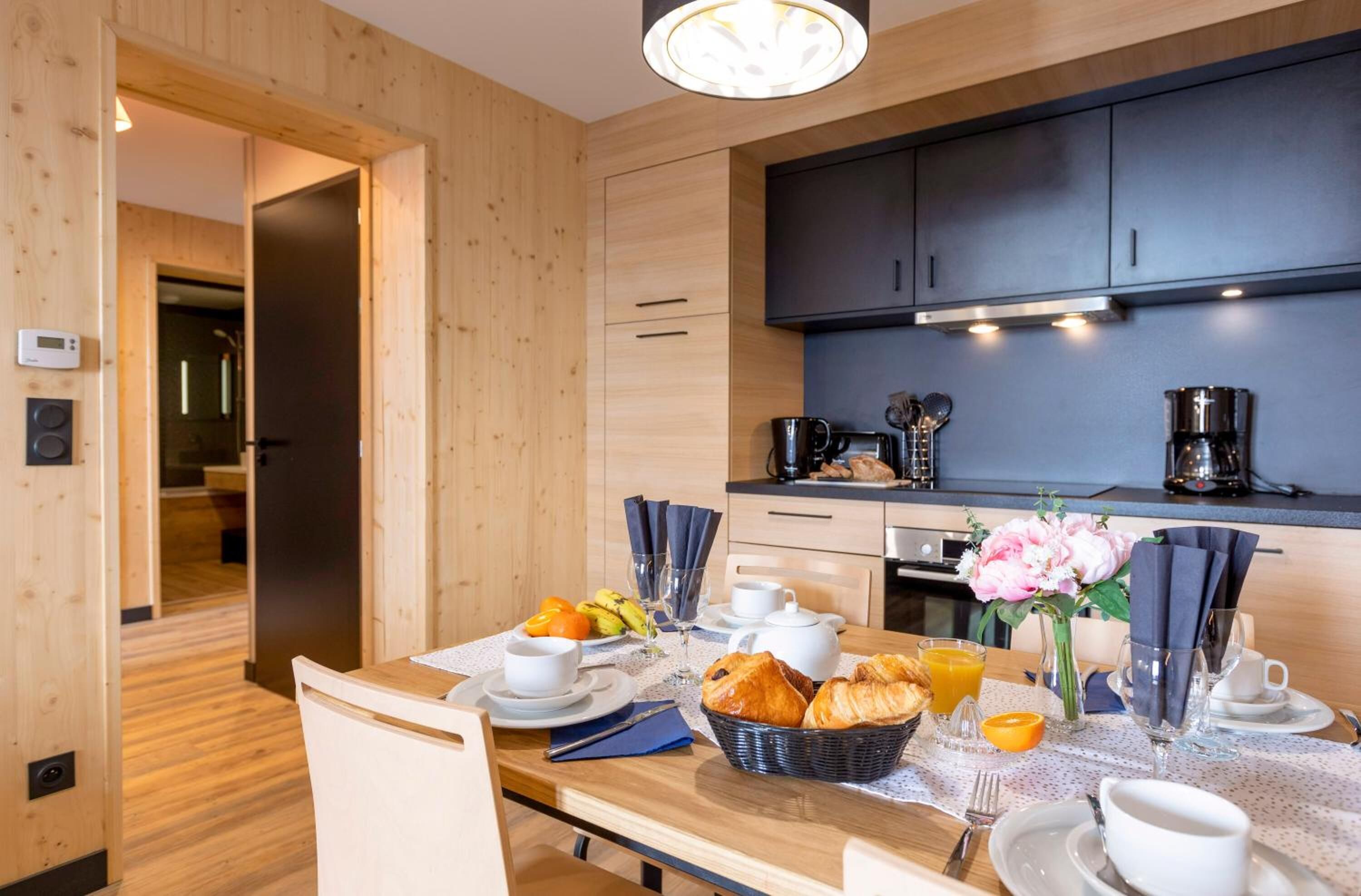 A modern kitchen with wooden cabinetry, a dining table set with breakfast, and a coffee machine.