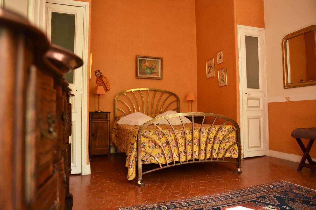 A bedroom with a curved bed, a wooden dresser, a nightstand, and a door.