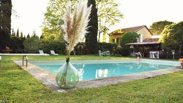 Une piscine agrémentée d’un vase en verre contenant des plumes d’herbe des pampas, le tout entouré de pelouse et d’arbres.