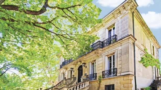 Un bâtiment historique doté d’une entrée imposante, d’un escalier menant à la porte principale et d’un balcon orné de rampes noires.