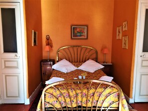 Una habitación con una cama, dos mesitas de noche, un reloj de pared y cuadros enmarcados.