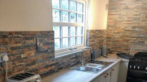 A compact kitchen with a stone backsplash, a window, a toaster, a sink, and a grill. - 4 Bedroom & 4 Bathroom House near St Neots (Saint Neots)