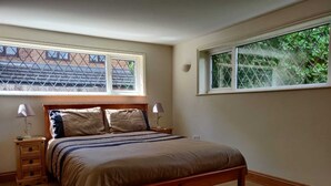 A bedroom with a wooden bed, two bedside tables, a window with a view of greenery, and a sloped ceiling. - 4 Bedroom & 4 Bathroom House near St Neots (Saint Neots)