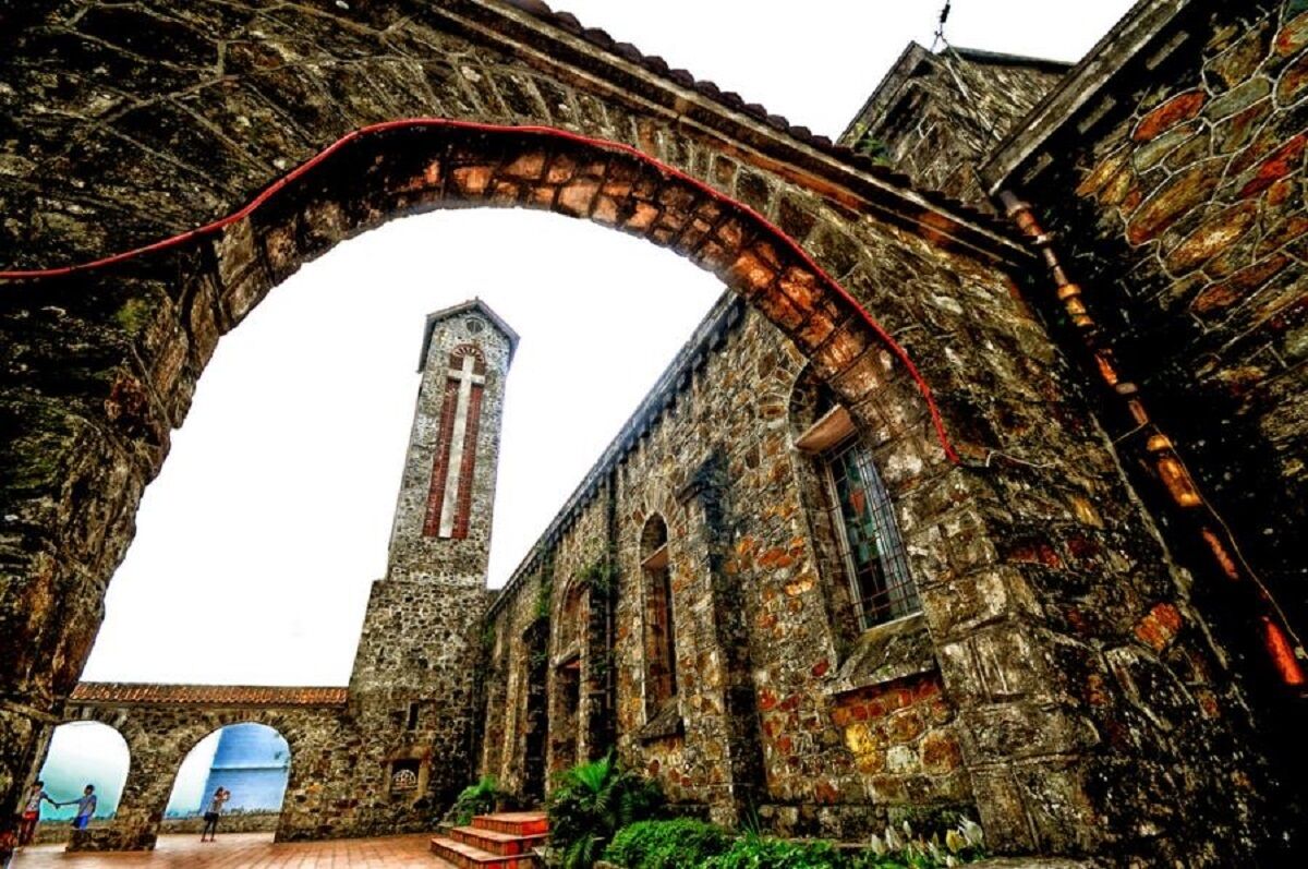 An old stone building with a large arched doorway and a tall tower with a cross.