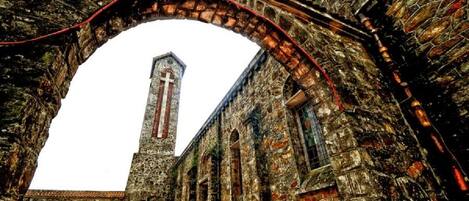 An old stone building with a large arched doorway and a tall tower with a cross.
