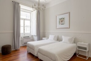 Een slaapkamer met twee bedden, een kroonluchter, een ingelijst kunstwerk en een raam met gordijnen.