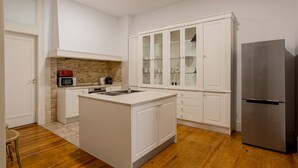 A modern kitchen with white cabinetry, a central island, a built-in microwave, and a stainless steel refrigerator. - JOIVY Astonishing 4BR home in Baixa,  5mins to Santa Justa Lift (Lisboa)