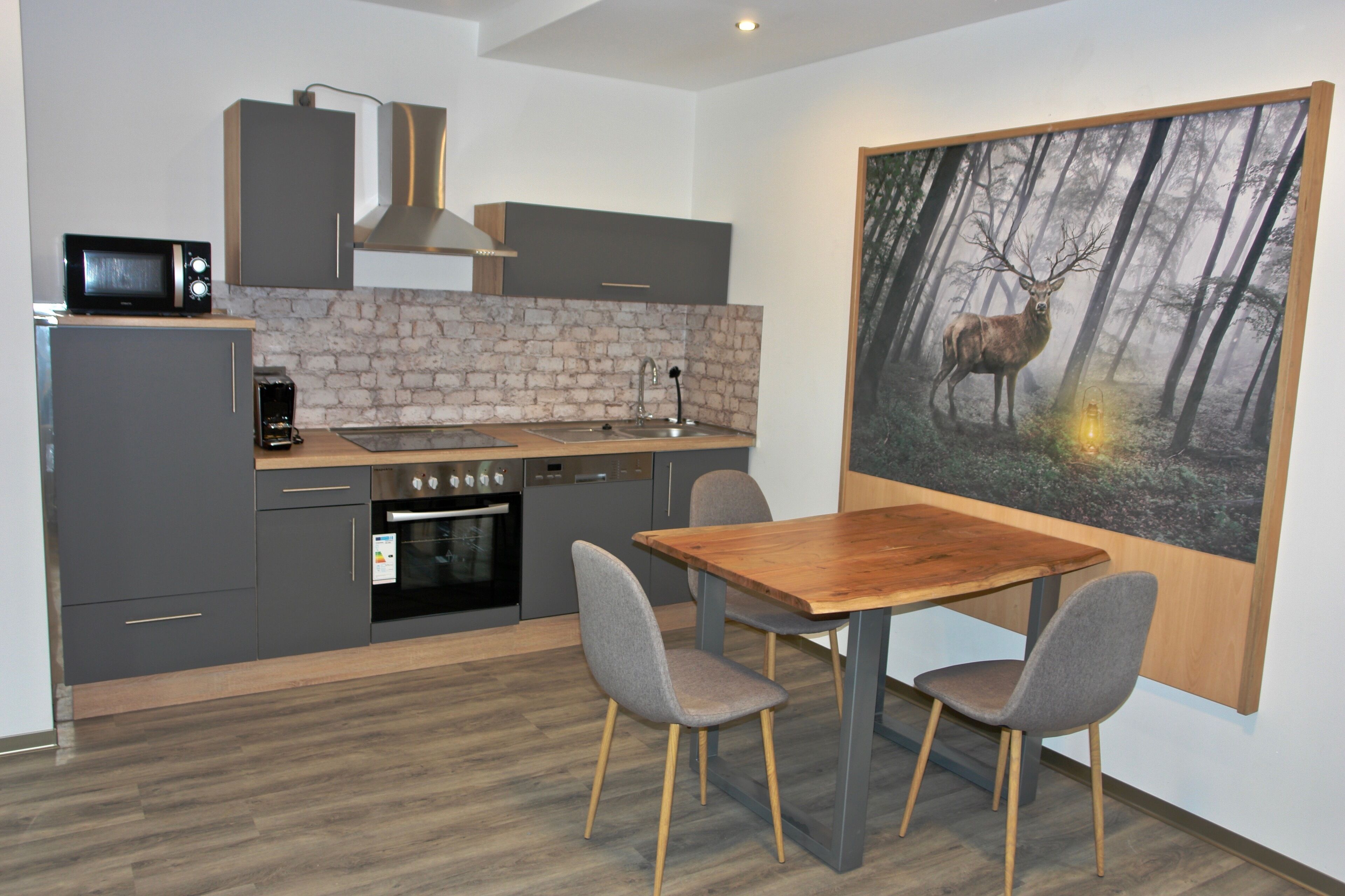 A modern kitchen with grey cabinets, a wooden countertop, and a large painting of a deer in a forest.