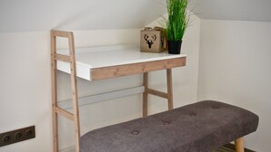 Una cama nido de madera con un banco al pie, un pequeño estante con una planta y una caja decorativa.