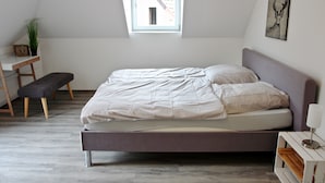 Un dormitorio con cama, banca, escritorio, planta y ventana.
