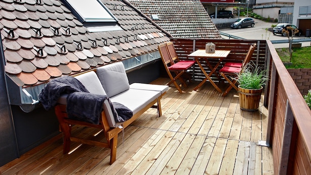 Una terraza de madera con un sofá, dos sillas rojas, una mesita y una planta en maceta.