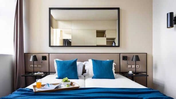 A hotel room with a large bed, two bedside tables, a nightstand, a mirror, and a tray with breakfast items. - JOIVY Spacious 1-bed Apt nearby Time Out Market &subway (Lisboa)