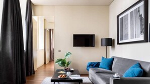 A modern living room with a grey sofa, blue cushions, a black coffee table, and a plant. A flat-screen TV is mounted on the wall, and a framed picture is above the sofa. - JOIVY Spacious 1-bed Apt nearby Time Out Market &subway (Lisboa)