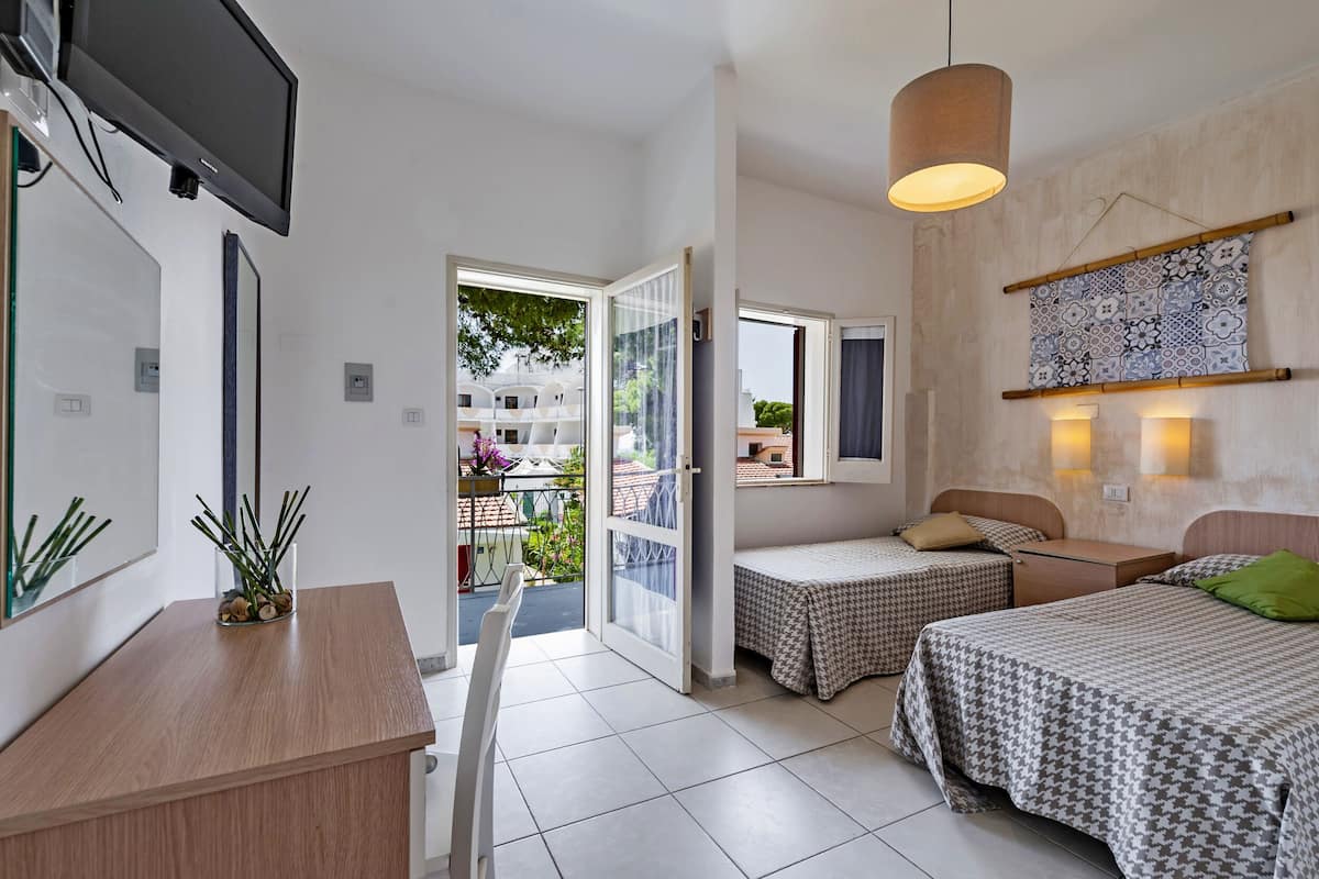 Habitación de hotel con cama, escritorio, televisión, balcón y vistas al exterior, además de un tapiz con motivos.