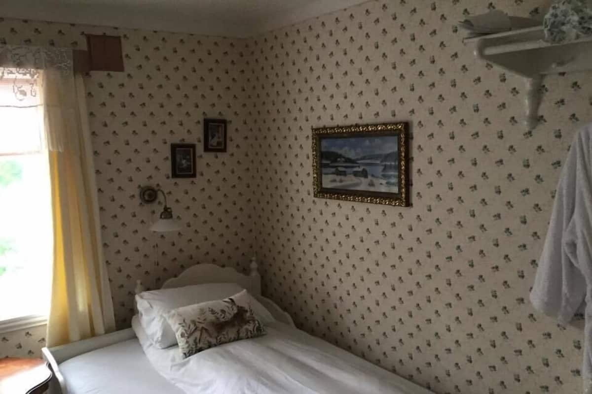Un dormitorio con una cama individual, una mesita de noche, cortinas en la ventana y un cuadro colgado en la pared.