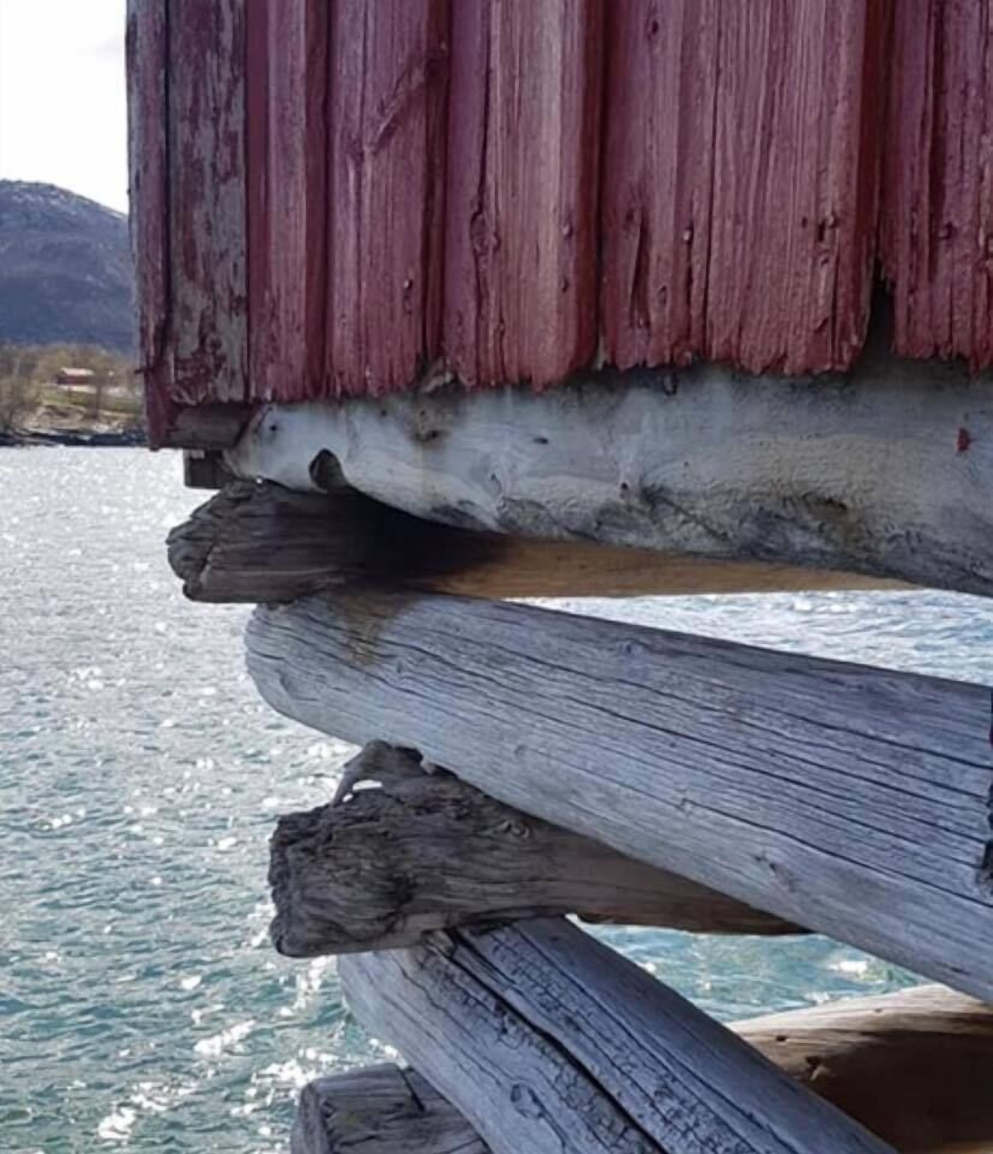 A wooden structure with a weathered appearance, possibly a dock or pier, extending over a body of water with a mountainous backdrop.