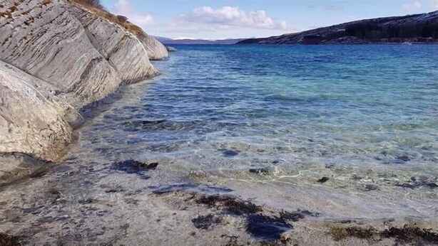 A coastal landscape with clear water, rocky cliffs, and a distant shoreline. - Skagen Gaard (Bodo)