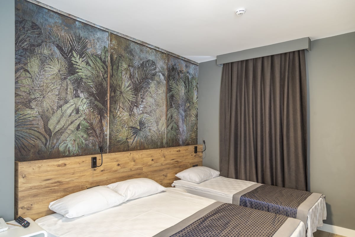 A hotel room with two beds, a large tropical mural on the wall, and a view of the outdoors.