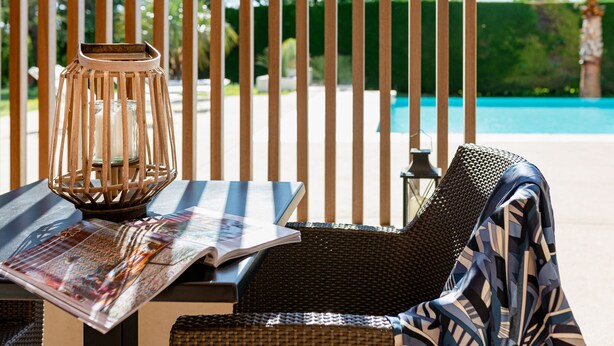 A lounge chair with a magazine, a candle in a metal holder, and a pool in the background. - La petite Aiguebonne (Allex)