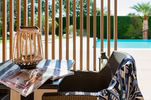 A lounge chair with a magazine, a candle in a metal holder, and a pool in the background. - La petite Aiguebonne (Allex)
