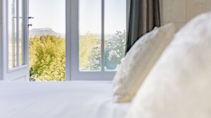 A bedroom with a large window, a bed, and a view of trees and a distant mountain. - La petite Aiguebonne (Allex)