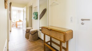 Un pasillo con suelo de madera, una consola de mimbre, un espejo y una puerta con pomo.