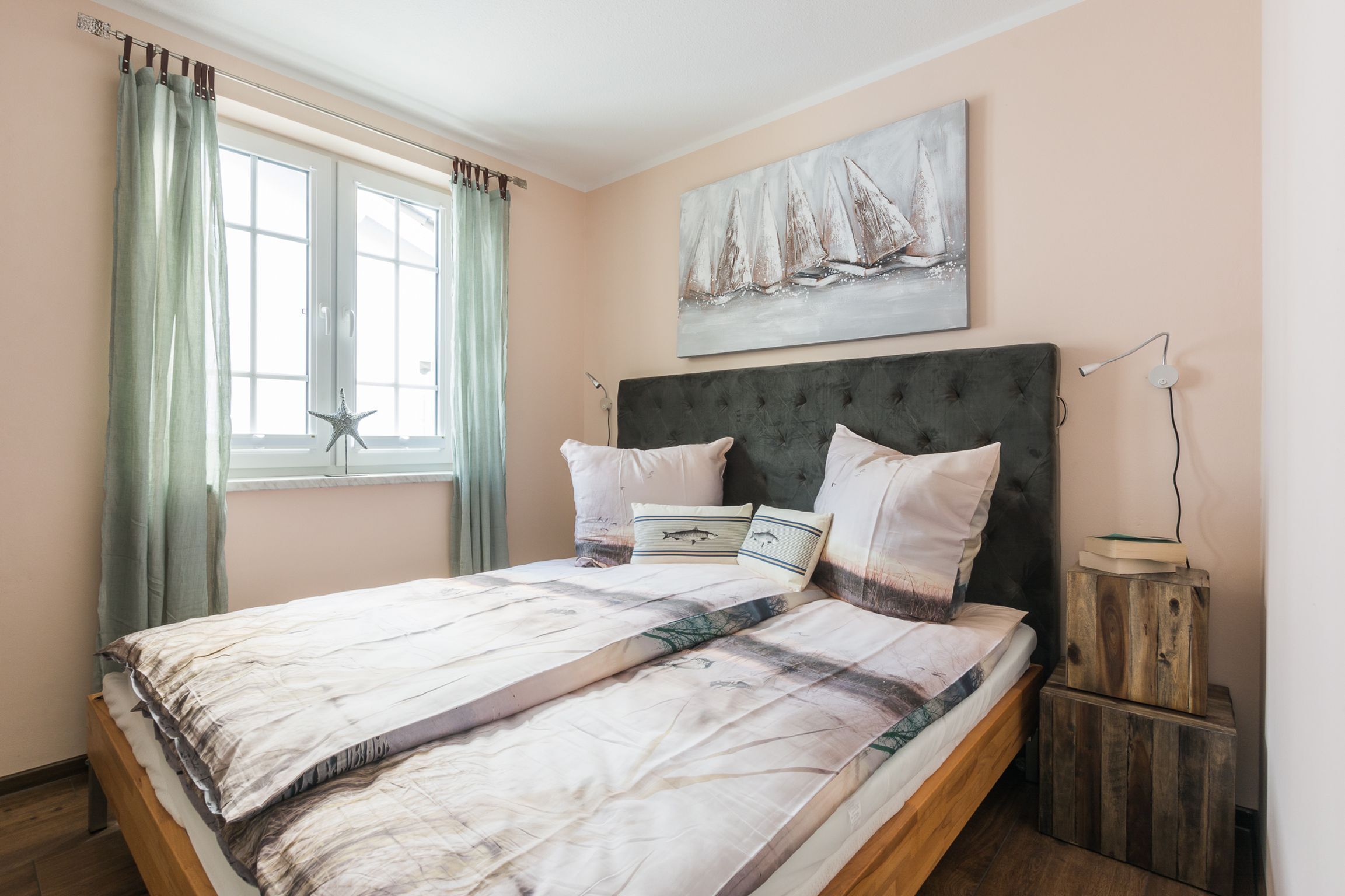 A bedroom with a bed, a starfish decoration, a sailboat painting, and a bedside table with a lamp.