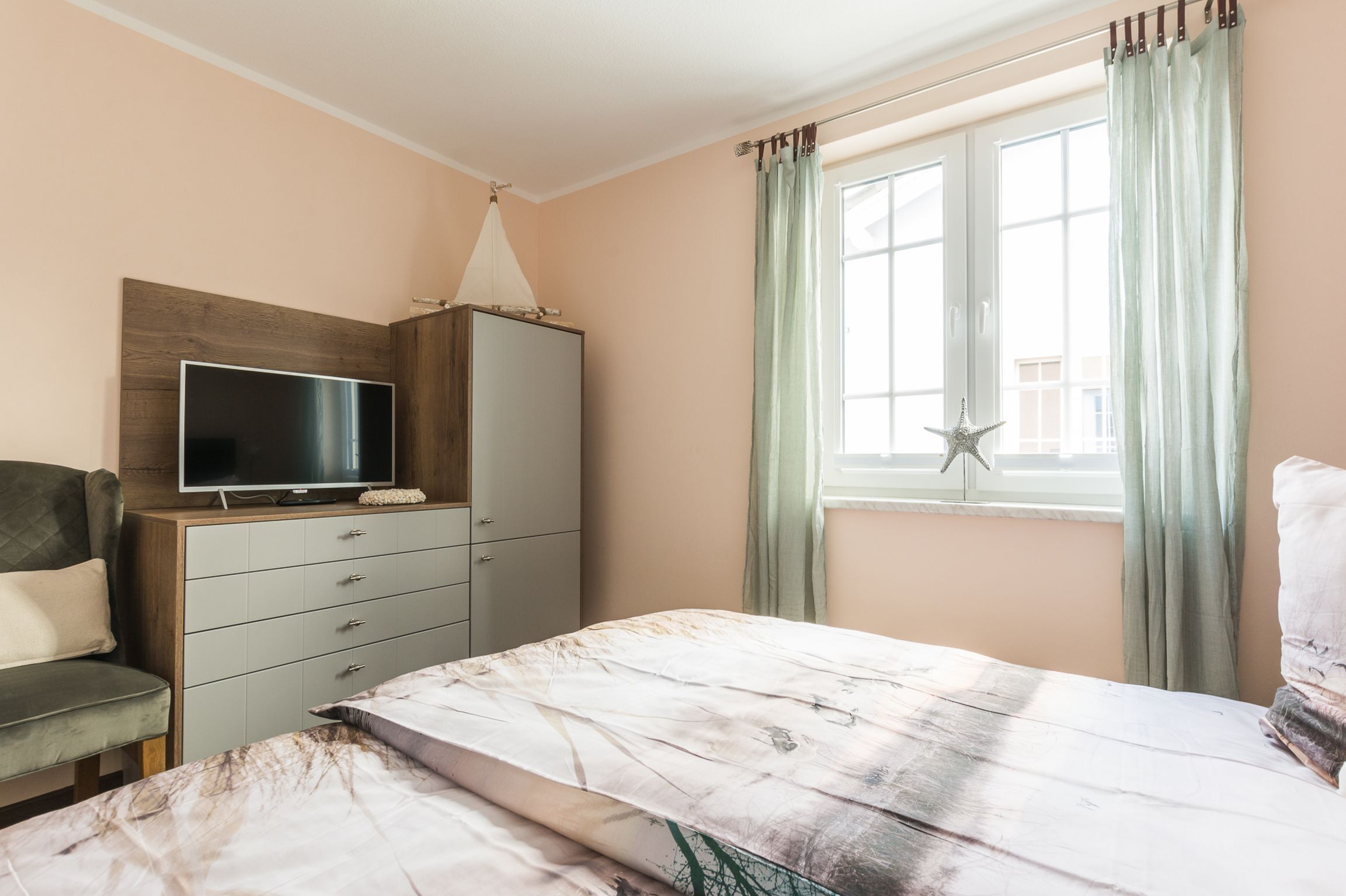 A bedroom with a bed, a TV on a wooden cabinet, a window with curtains, and a star decoration.