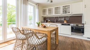 Una cocina con armarios blancos, una mesa de madera, sillas de mimbre y un horno.