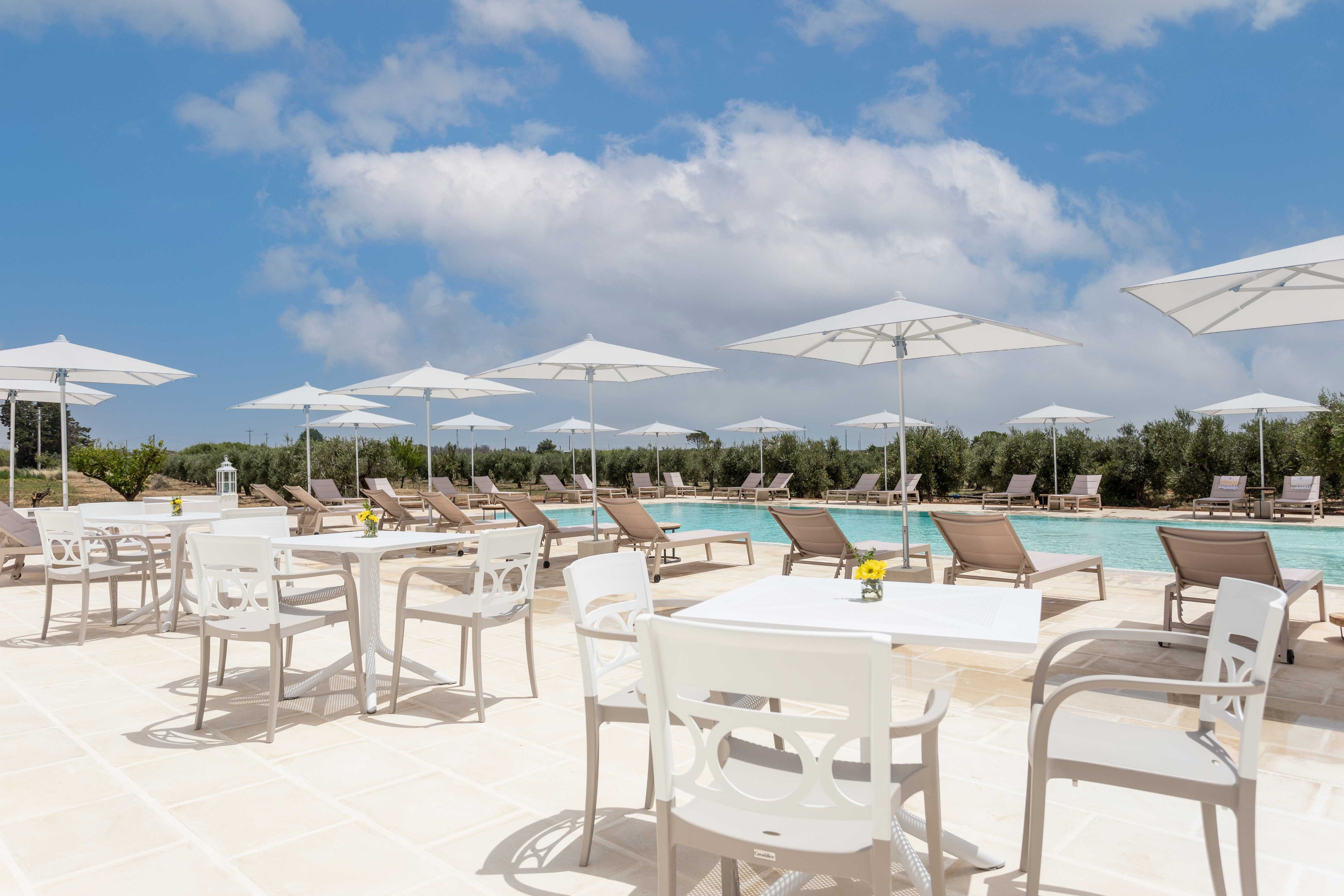 A poolside area with lounge chairs and umbrellas, a pool, and a clear sky.