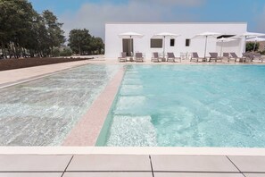 A swimming pool with clear water, surrounded by lounge chairs and umbrellas, and a building with white walls in the background. - Palummare Agri Hotel (Alliste)