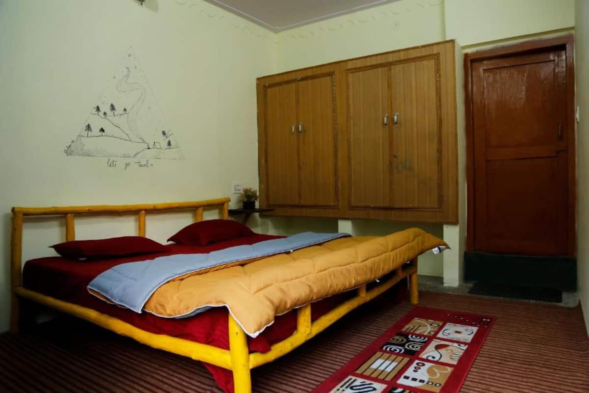 A bedroom with a bed, wooden wardrobe, and a wall with a drawing.