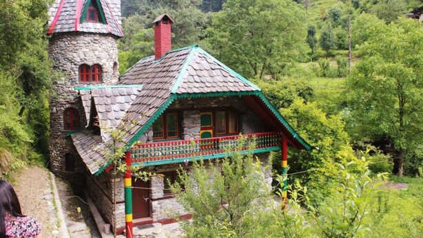 A rustic stone house with a red chimney, a wooden balcony, and a steeply pitched roof. - The Hostalgic Jibhi - Hostel (Banjar)