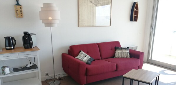 A red sofa with patterned cushions, a coffee maker, a kettle, a lamp, and a small table. - Facing the sea - Balcony - Studio for 2 (La Baule-Escoublac)
