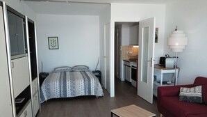 Una habitación pequeña con cama, una mesita, un sofá y una kitchenette.