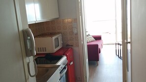 Una cocina compacta con armarios blancos, un microondas, un horno rojo y un teléfono.