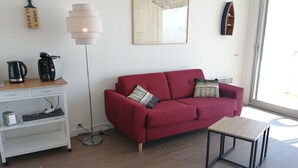 Una sala de estar moderna con un sofá rojo, una mesita de madera, una lámpara de pie y una cafetera sobre un estante de madera.