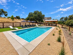 A rectangular swimming pool with a clear blue water surface, surrounded by a wooden deck and a gravel area with small plants.