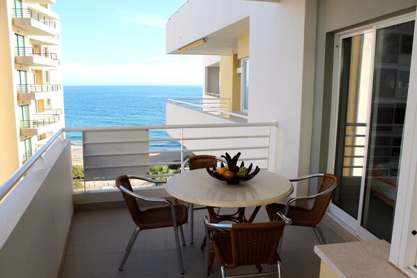 Ein Balkon mit Tisch und Stühlen mit Blick auf das Meer.