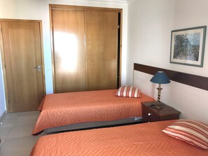 Una habitación de hotel con dos camas, un armario de madera, una mesita de noche con una lámpara y un cuadro enmarcado en la pared.