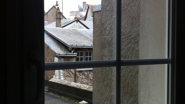 Une fenêtre donnant sur l’extérieur d’un bâtiment, avec vue sur un mur en briques et un toit.