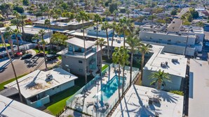 A high-rise building with multiple balconies, a rooftop pool, and surrounding palm trees. - Walkable Old Town Scottsdale, Heated Poolside Mid Century Condo. (Scottsdale)