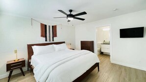 A bedroom with a bed, a nightstand, a ceiling fan, a TV, and a bathroom visible through an open door. - Walkable Old Town Scottsdale, Heated Poolside Mid Century Condo. (Scottsdale)