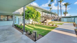 Un edificio moderno con un paseo techado, una escalera y un césped cuidado con palmeras.