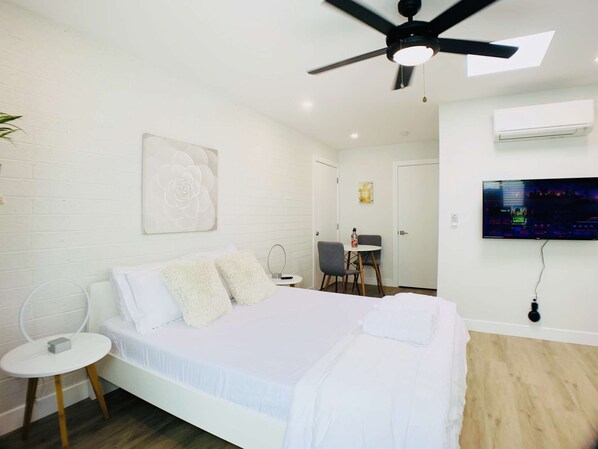Ein modernes Schlafzimmer mit Bett, Deckenventilator, Fernseher und einem kleinen Tisch mit Stuhl.