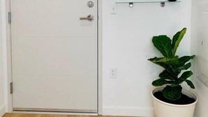 A white door with a silver handle, a round mirror on a wall-mounted shelf, and a potted plant beside the door. - Unique poolside studio -  less than a mile to Old Town (Scottsdale)