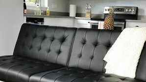 A black leather sofa in a modern kitchen with white cabinets, a stainless steel oven, and a pineapple on the counter. - Birdhouse on Green Lake (Seattle)