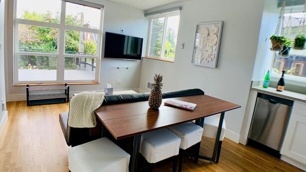 A modern kitchen with a dining table, a television, and a view of the outdoors. - Birdhouse on Green Lake (Seattle)