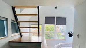 A bedroom with a loft bed, a window with a view of greenery, and a desk area. - Birdhouse on Green Lake (Seattle)