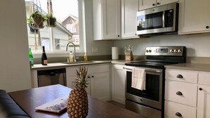 A kitchen with white cabinets, a microwave, an oven, and a wooden table with a pineapple. - Birdhouse on Green Lake (Seattle)